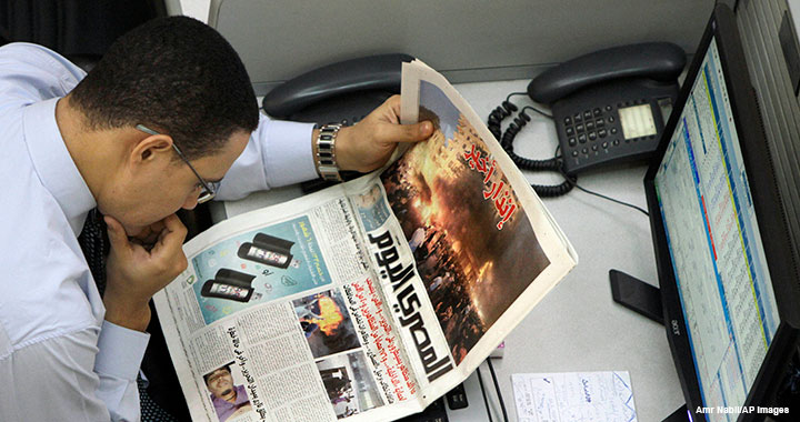 An Egyptian trader reads a local newspaper, which features coverage of clashes between protesters and security forces, at the Egyptian stock exchange in Cairo on 20 November 2011.